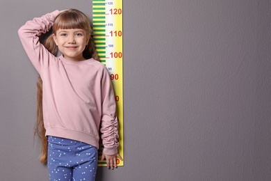 Little girl measuring her height on grey background