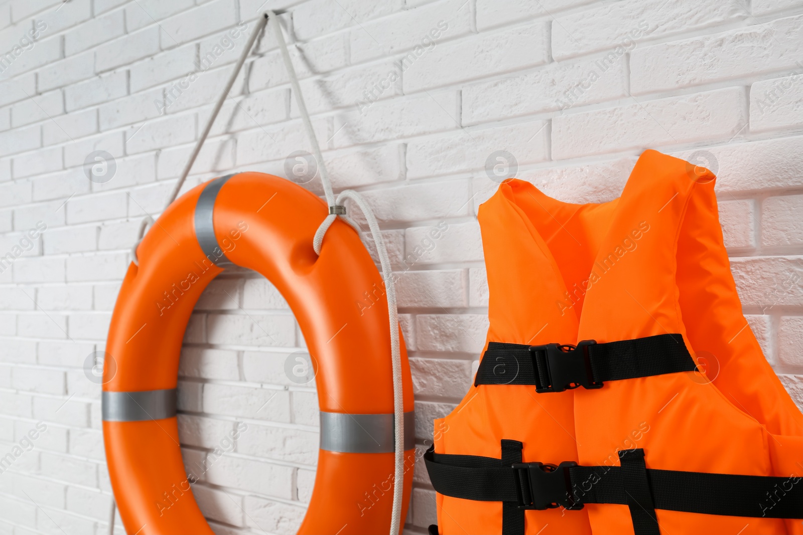 Photo of Orange life jacket and lifebuoy on white brick wall. Rescue equipment