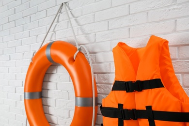 Orange life jacket and lifebuoy on white brick wall. Rescue equipment