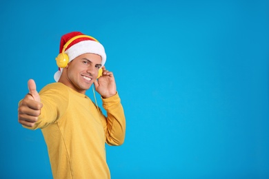 Photo of Happy man with headphones on blue background, space for text. Christmas music