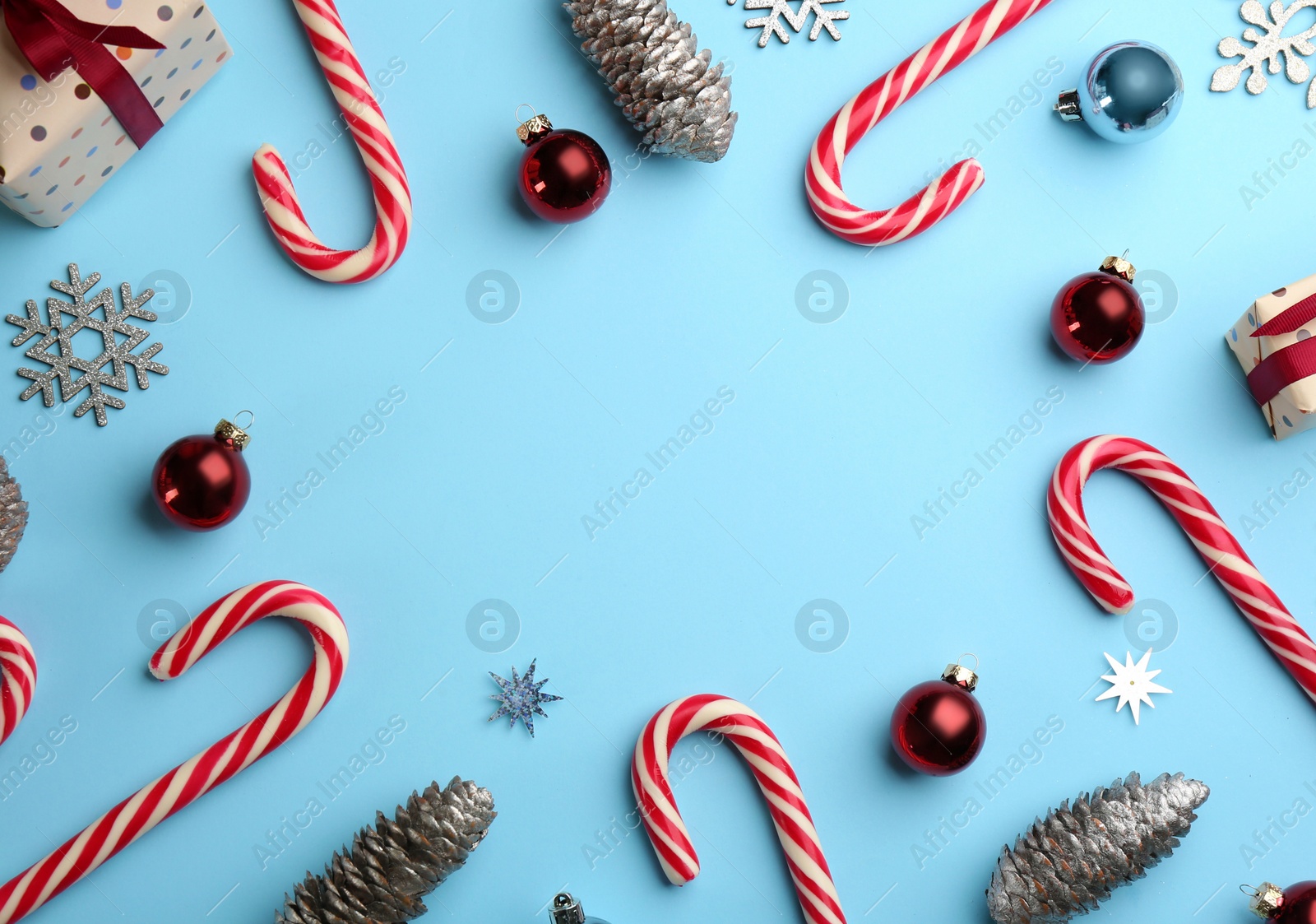 Photo of Frame of candy canes and Christmas decor on light blue background, flat lay. Space for text
