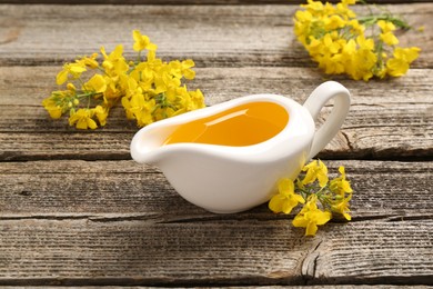 Photo of Rapeseed oil in gravy boat and beautiful yellow flowers on wooden table
