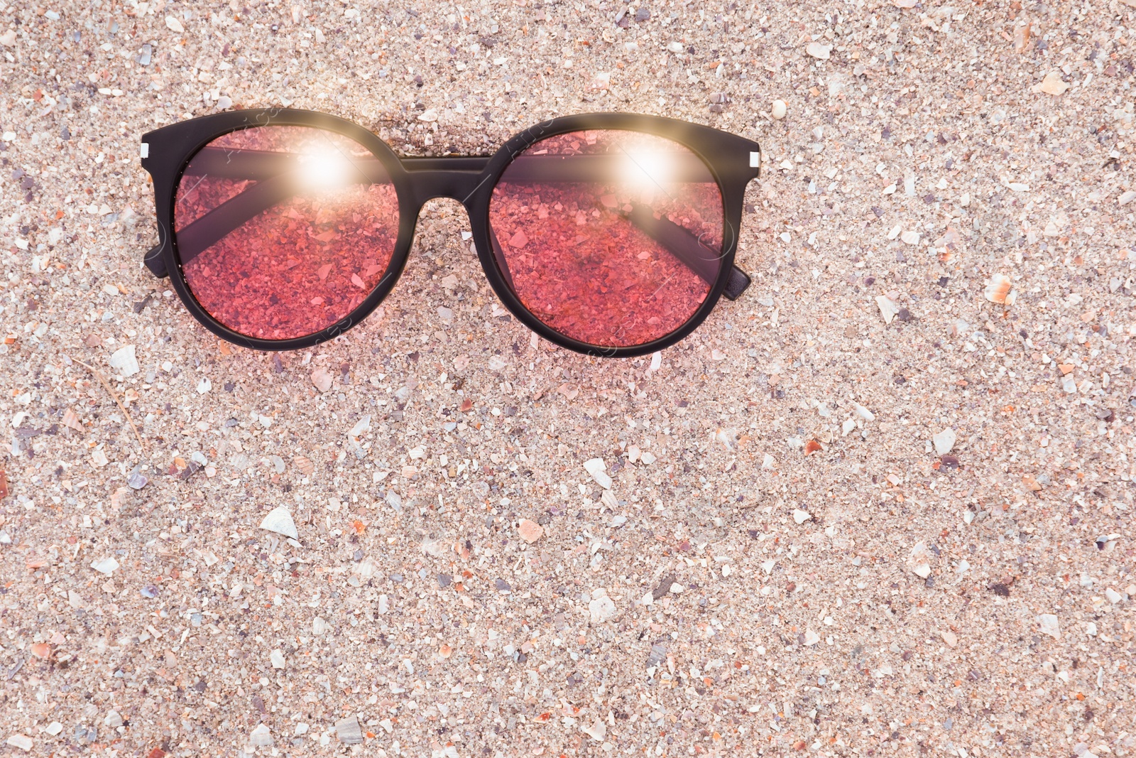 Photo of Stylish sunglasses on sandy beach, top view. Space for text