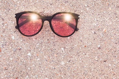 Stylish sunglasses on sandy beach, top view. Space for text