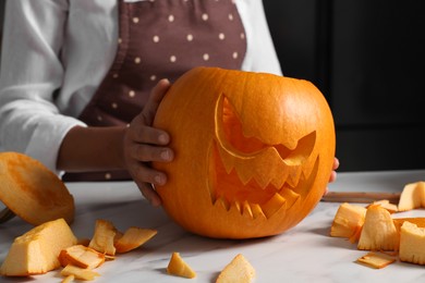 Photo of Woman carving pumpkin for Halloween at white marble table, closeup