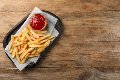 Delicious french fries served with ketchup on wooden table, top view. Space for text