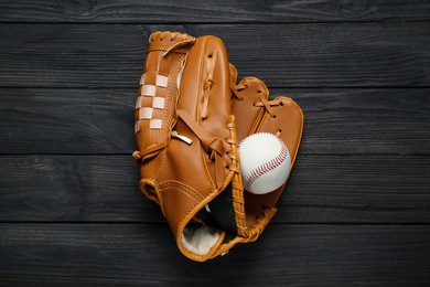 Photo of Catcher's mitt and baseball ball on black wooden table, top view. Sports game