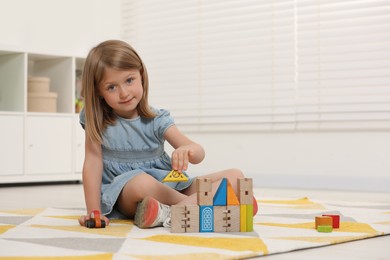 Cute little girl playing with wooden toys indoors, space for text