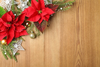 Photo of Flat lay composition with poinsettias (traditional Christmas flowers) and holiday decor on wooden table. Space for text