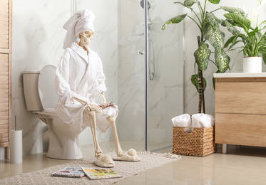 Photo of Skeleton in bathrobe with mobile phone sitting on toilet bowl