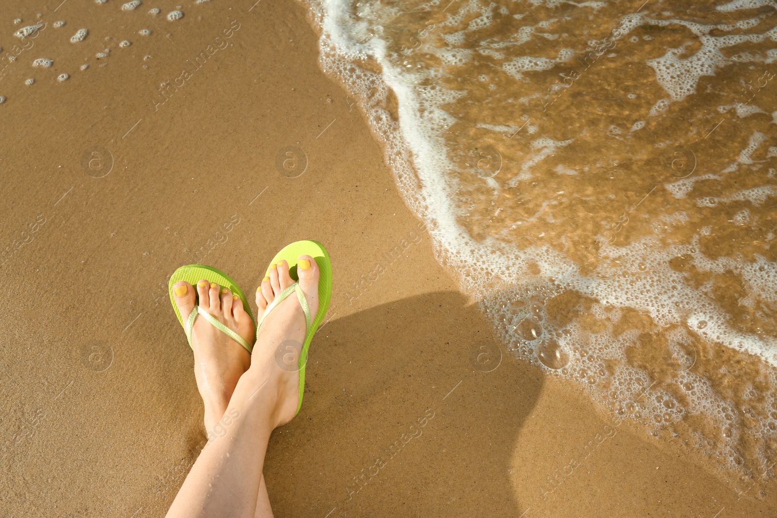 Photo of Closeup of woman with flip flops on sand near sea, space for text. Beach accessories