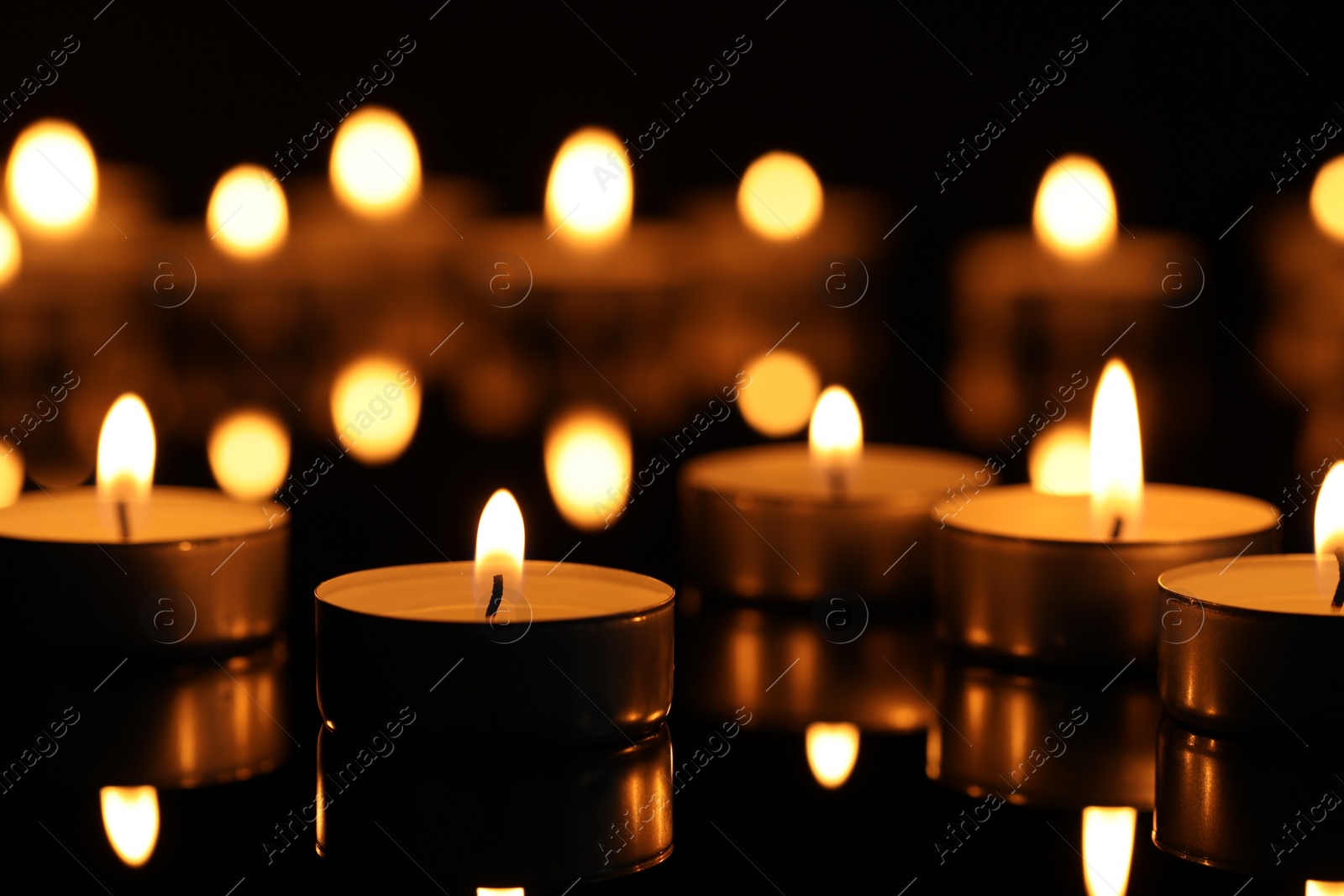 Photo of Burning candles on surface in darkness, closeup