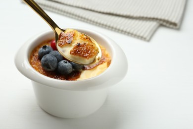 Photo of Eating delicious creme brulee with berries from spoon at white table, closeup. Space for text