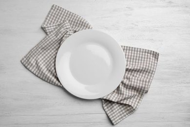 Photo of Empty plate and napkin on white wooden background, flat lay