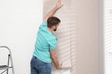 Photo of Man hanging stylish wall paper sheet indoors