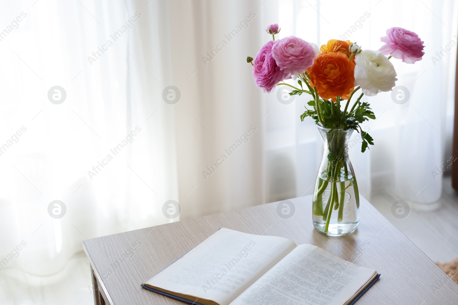 Photo of Bouquet of beautiful ranunculus flowers in vase and open book on wooden table indoors. Space for text