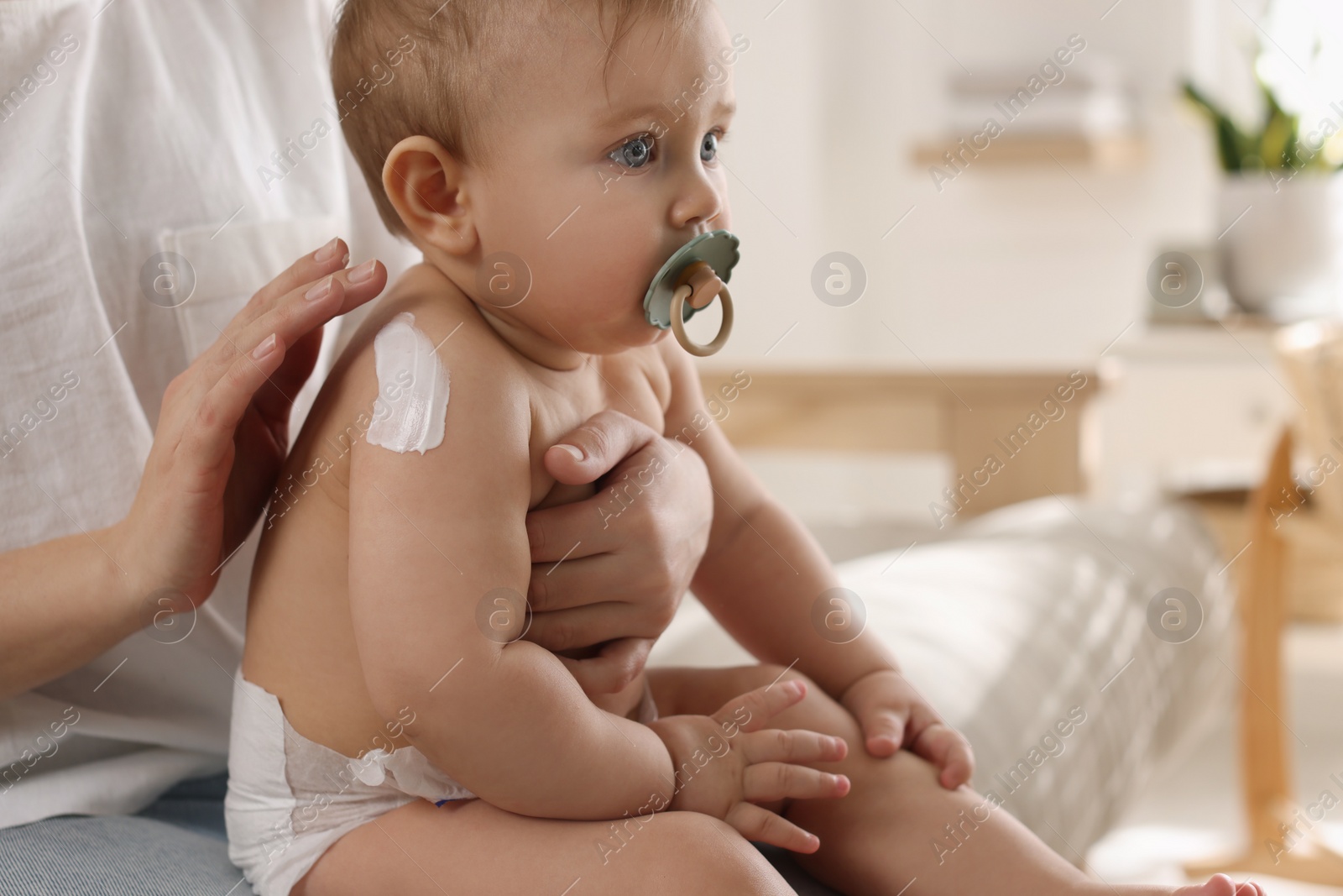 Photo of Mother applying body cream on her little baby at home, closeup