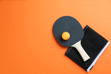 Photo of Ping pong racket, net and ball on orange background, flat lay. Space for text