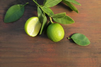 Branch with fresh leaves and limes on wooden table, closeup