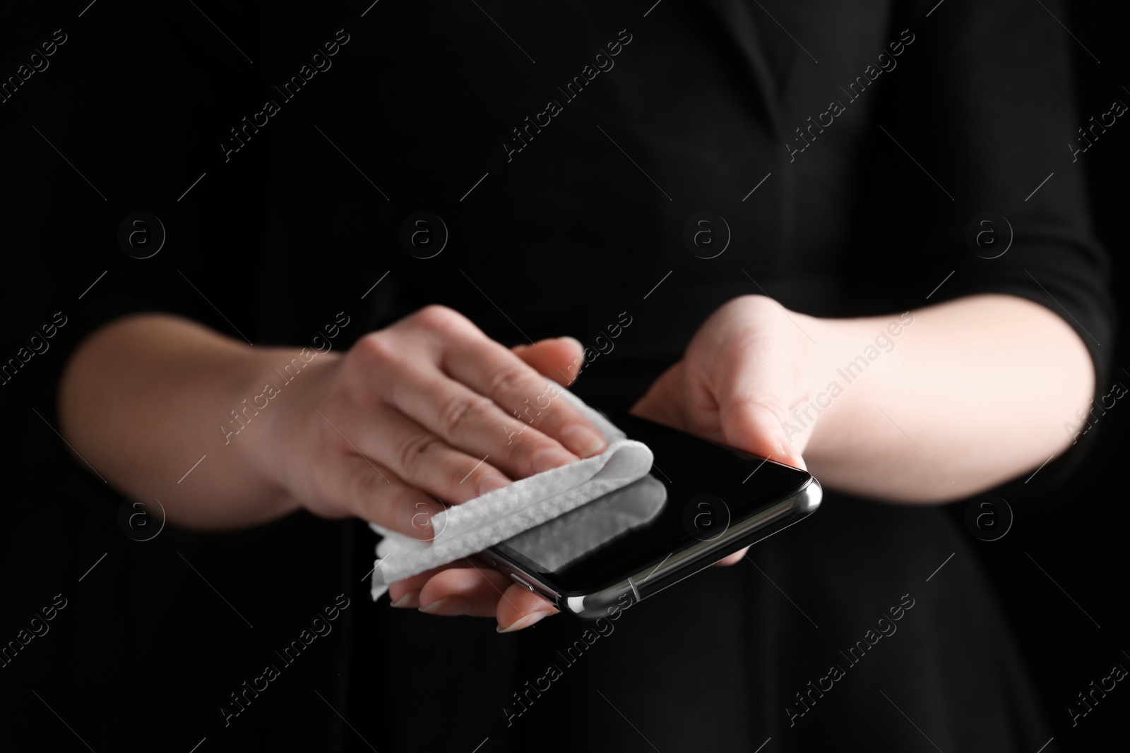 Photo of Woman cleaning mobile phone with antiseptic wipe on black background, closeup