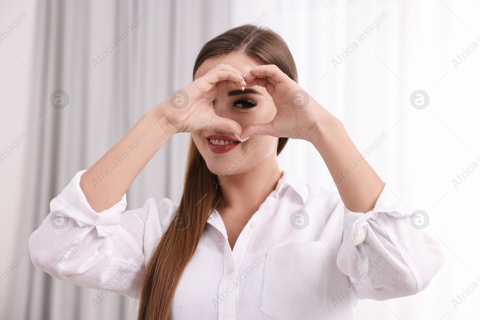 Photo of Happy woman showing heart gesture with hands indoors