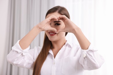 Happy woman showing heart gesture with hands indoors