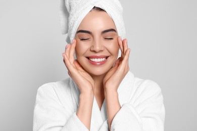 Young woman in bathrobe with towel on light grey background. Spa treatment