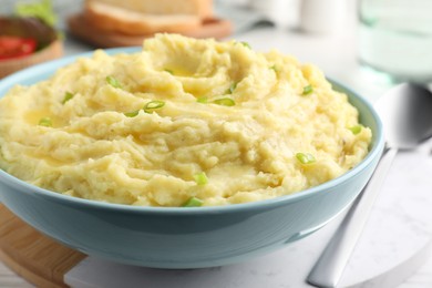 Photo of Bowl of tasty mashed potatoes with onion served on white wooden table, closeup