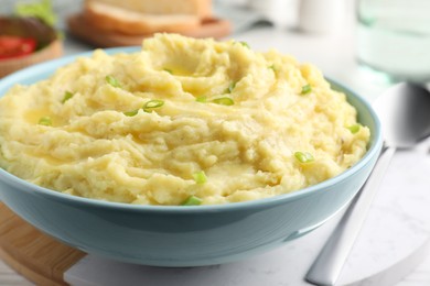 Bowl of tasty mashed potatoes with onion served on white wooden table, closeup