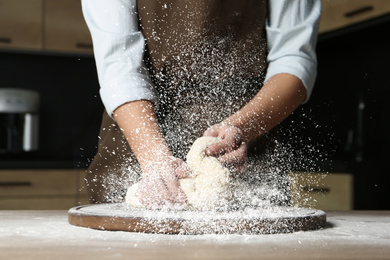 Image of Young woman kneading dough at table in kitchen, closeup