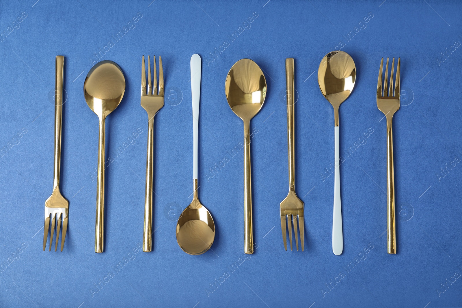 Photo of Set of new gold cutlery on blue background, flat lay