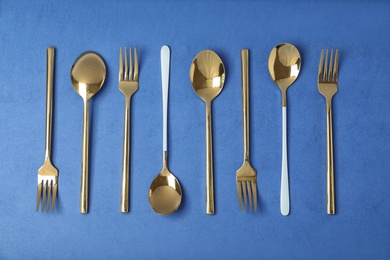 Set of new gold cutlery on blue background, flat lay