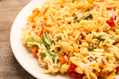 Photo of Tasty rice pilaf with vegetables on wooden table, closeup