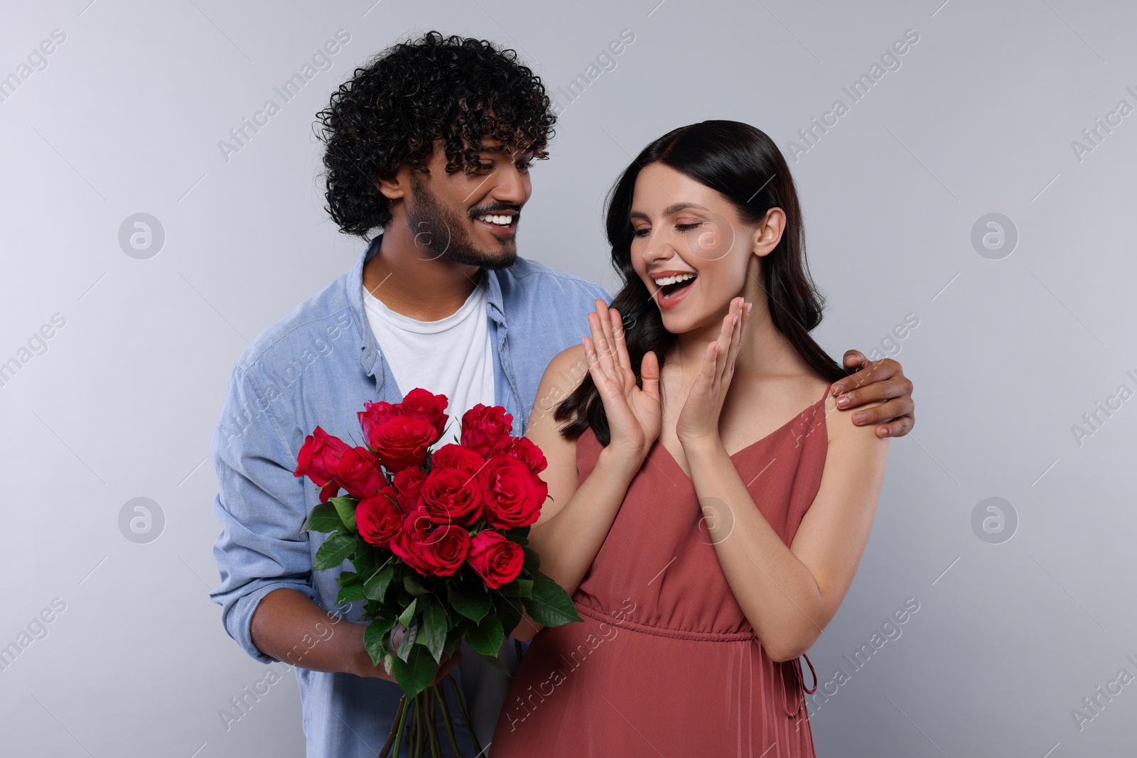 Photo of International dating. Handsome man presenting roses to his beloved woman on light grey background