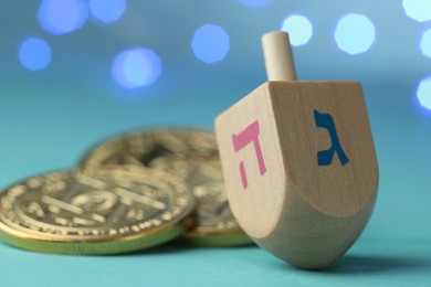 Photo of Hanukkah celebration. Wooden dreidel with jewish letters and coins against light blue background with blurred lights, closeup. Space for text