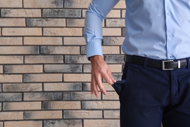Businessman showing empty pocket near brick wall, closeup. Space for text