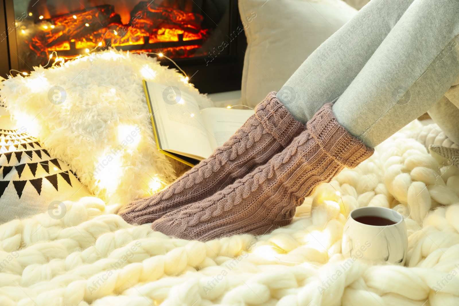 Photo of Woman with cup of tea sitting on soft plaid near fireplace, closeup