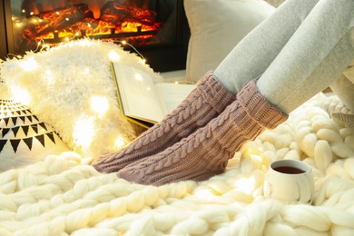 Woman with cup of tea sitting on soft plaid near fireplace, closeup