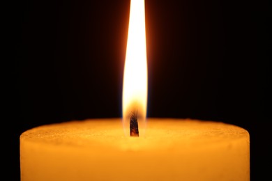 Burning wax candle on black background, closeup