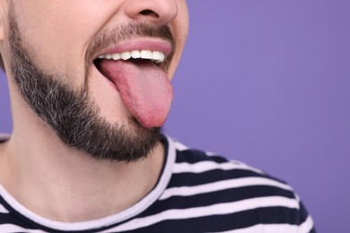 Photo of Happy man showing his tongue on purple background, closeup. Space for text