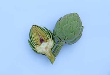 Cut and whole fresh raw artichokes on light blue background, flat lay