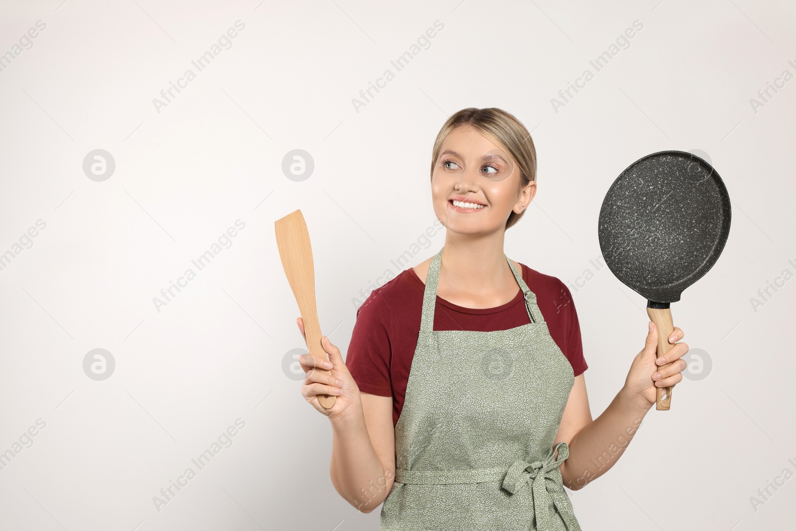 Photo of Beautiful young woman in clean apron with kitchen tools on light grey background