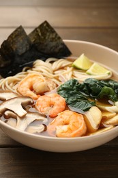 Delicious ramen with shrimps and mushrooms in bowl on wooden table, closeup. Noodle soup