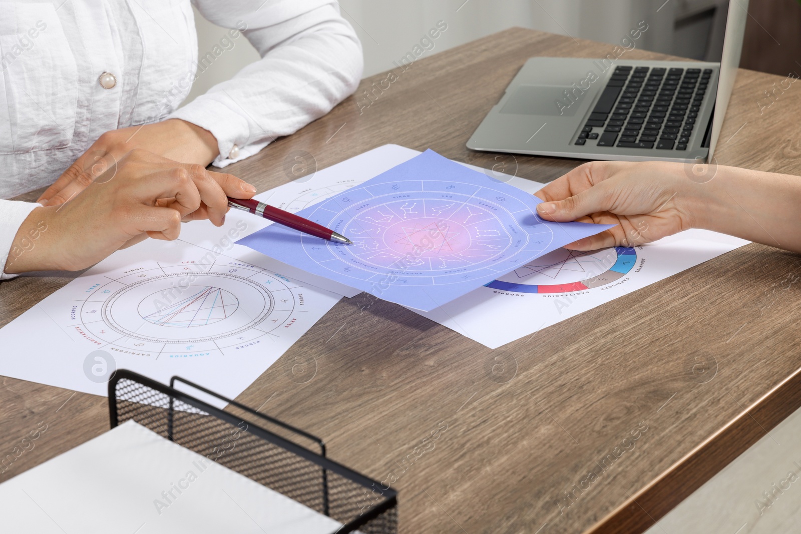 Photo of Astrologer showing zodiac wheel to client at wooden table indoors, closeup