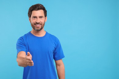 Photo of Happy man welcoming and offering handshake on light blue background. Space for text