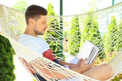 Photo of Man with book relaxing in hammock outdoors on warm summer day