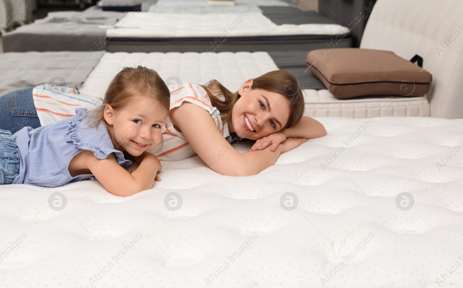 Photo of Mother and her daughter lying on new orthopedic mattress in store