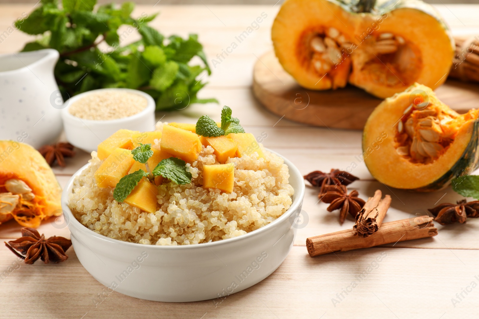 Photo of Tasty quinoa porridge with pumpkin, mint in bowl and spices on light wooden table