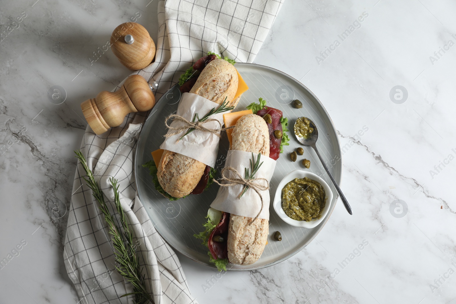 Photo of Delicious sandwiches with bresaola, cheese and lettuce served on white marble table, flat lay