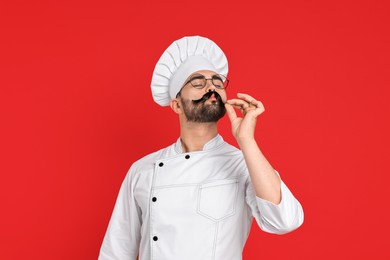 Professional chef with funny artificial moustache showing perfect sign on red background